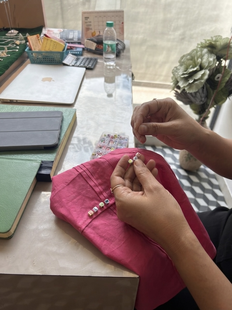 Hand-stringing letter beads onto a pink cotton shirt cuff